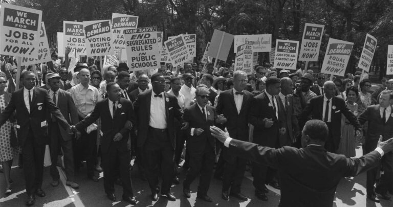 Famous figures of the March on Washington hold signs and walk with linked arms