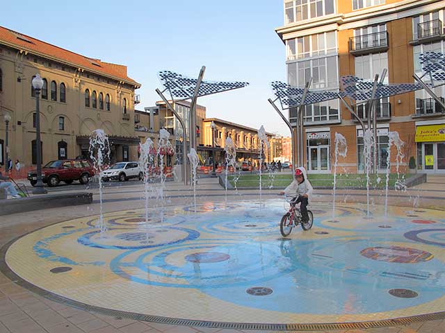 A child rides a bike through a spray-ground water park in Columbia Heights
